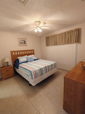A bedroom with a bed, nightstand, lamp, ceiling fan, window with curtains, and a picture on the wall. - Parkside Paradise (Inverness)