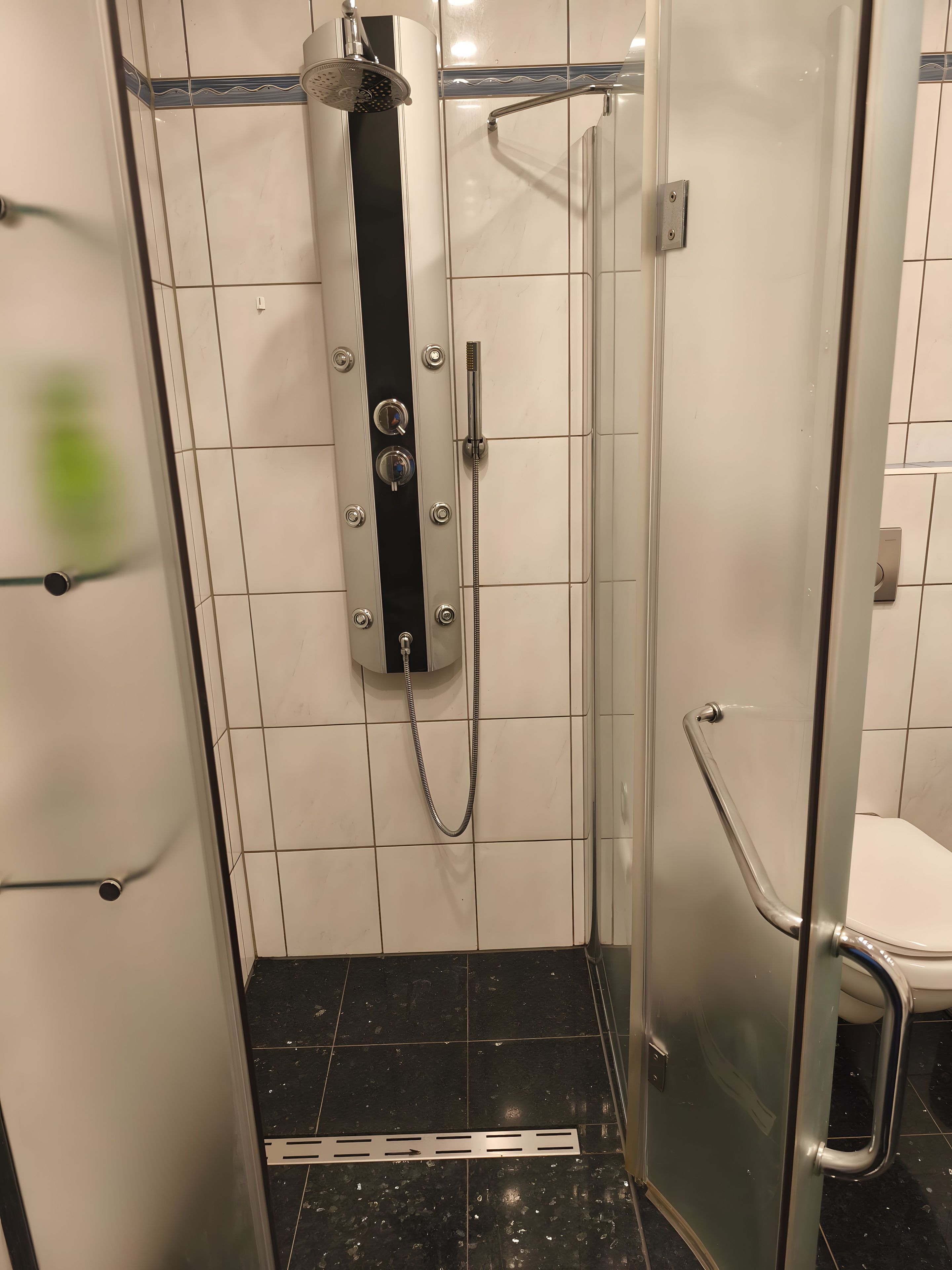Cabina de ducha con mampara de vidrio, cabezal de ducha de mano, panel de control y manguera para ducha de mano.