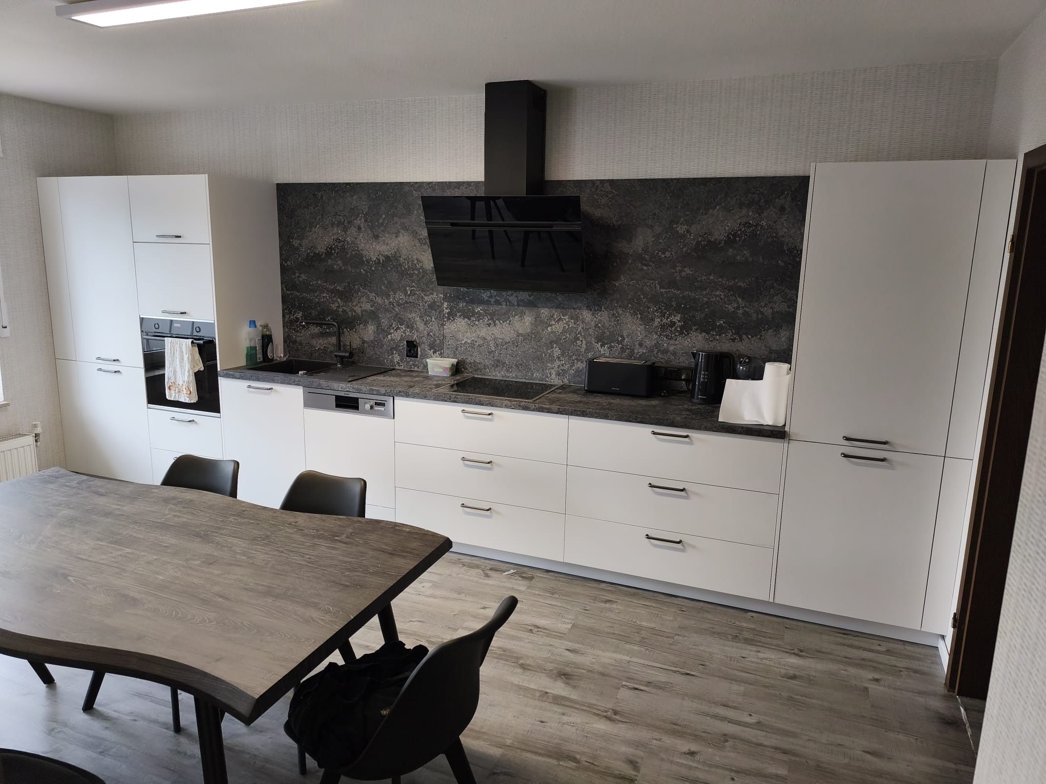 Eine moderne Küche mit weißen Schränken, einer dunklen Spritzschutzwand und einem eingebauten Backofen.