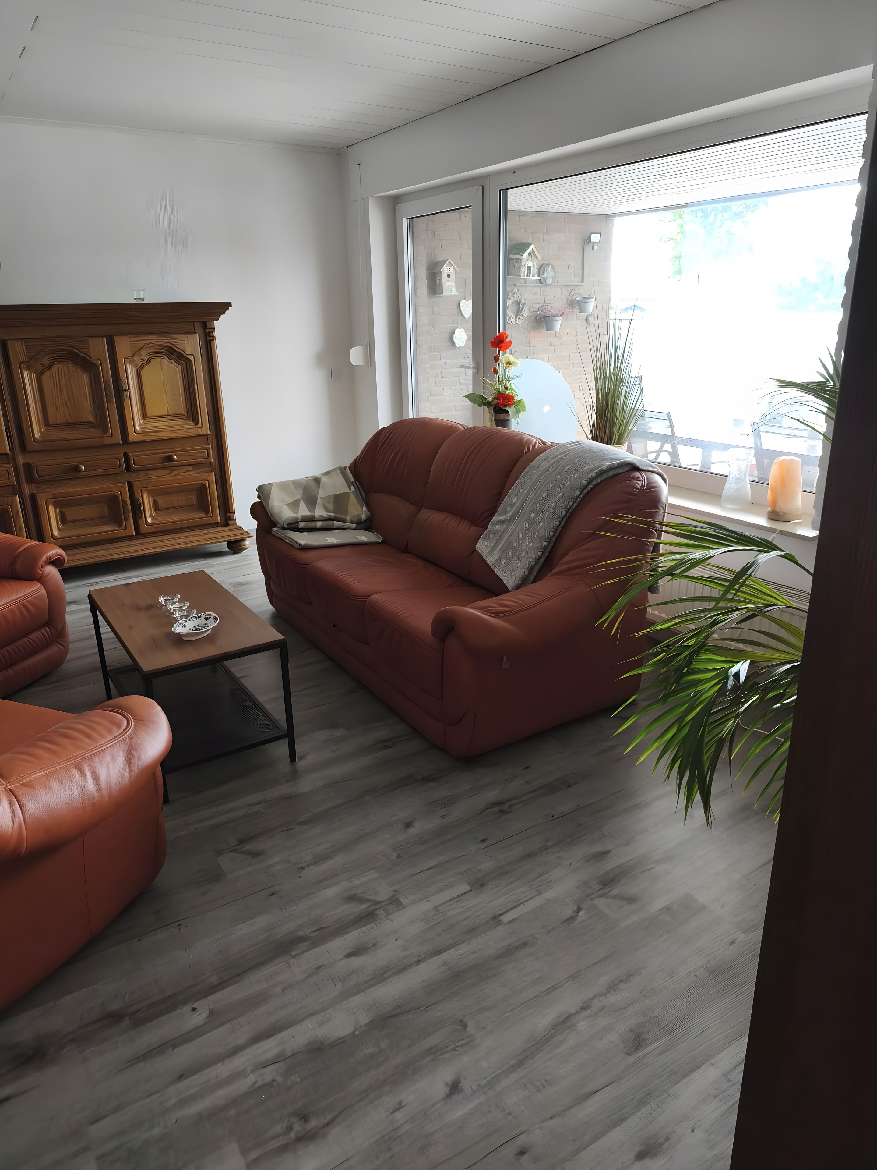A living room with a brown leather sofa, a wooden cabinet, and a small table.