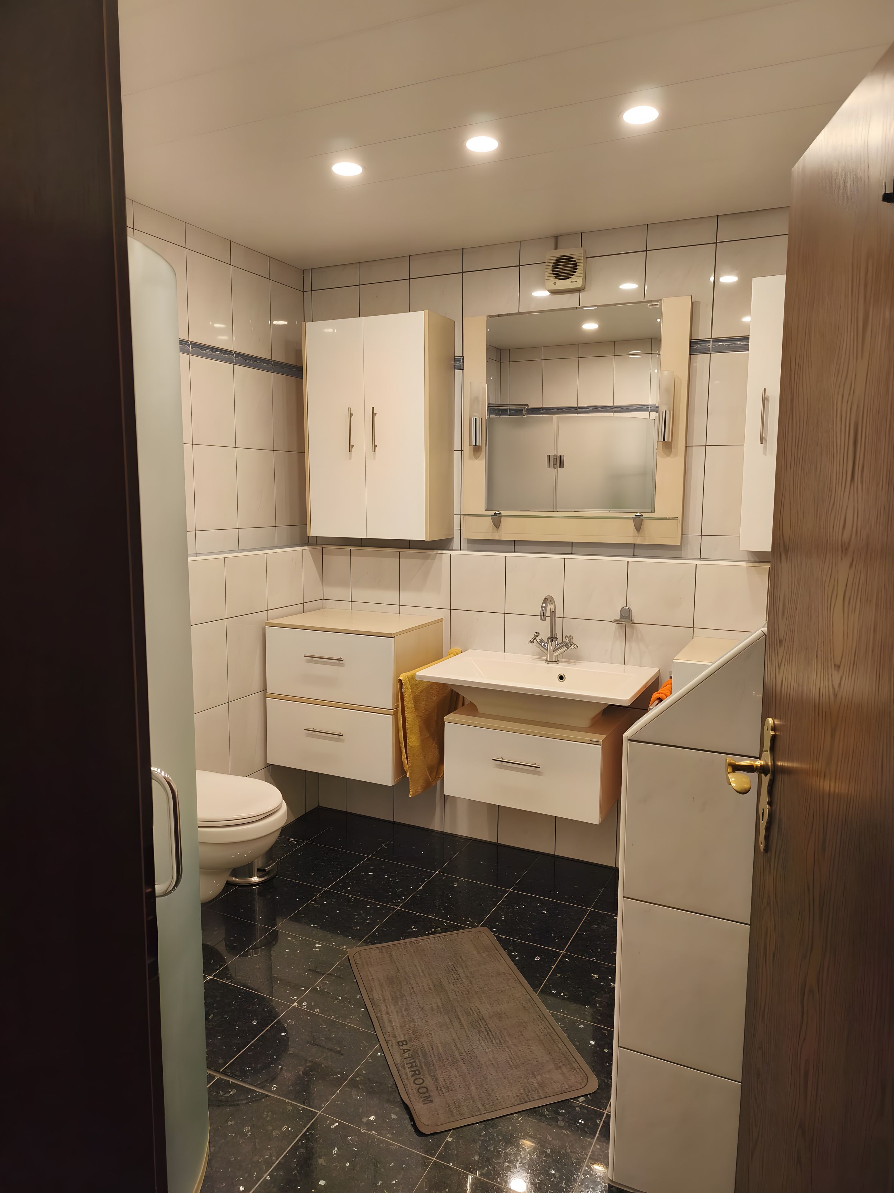 Un baño moderno con inodoro, lavabo, espejo y armarios.
