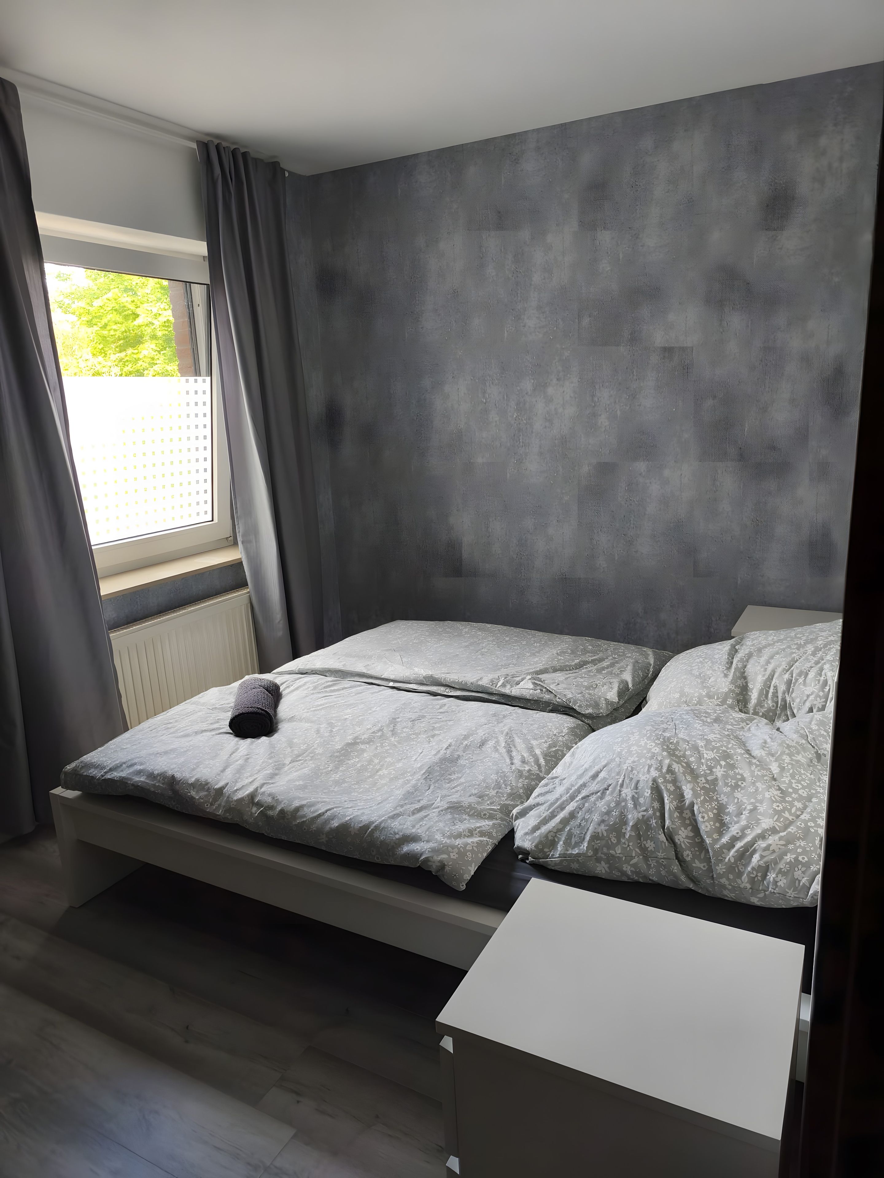 Ein Zimmer mit einem Bett, einem Vorhangfenster und einer Heizung.