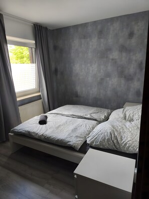 Ein Zimmer mit einem Bett, einem Vorhangfenster und einer Heizung.