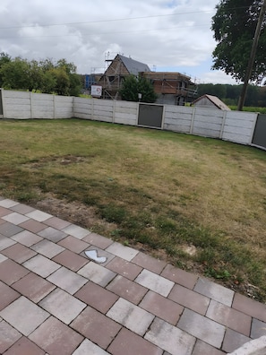 Eine gepflasterte Terrasse mit Rasenfläche und einem Metallzaun.