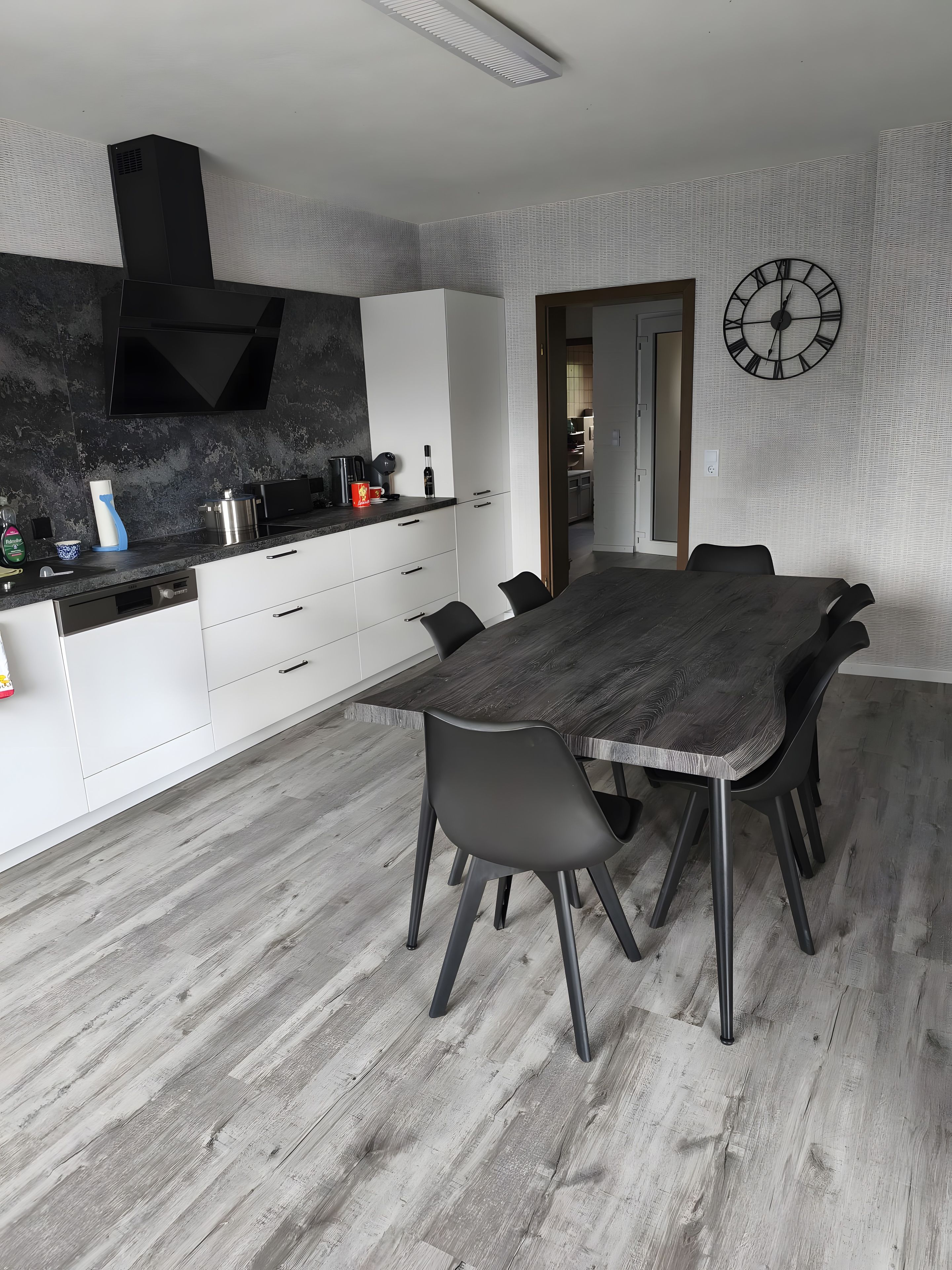Una cocina moderna con armarios blancos, una campana extractora negra y un comedor con una gran mesa y sillas de madera.