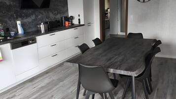 Una cocina moderna con armarios blancos, una campana extractora negra y un comedor con una gran mesa y sillas de madera.