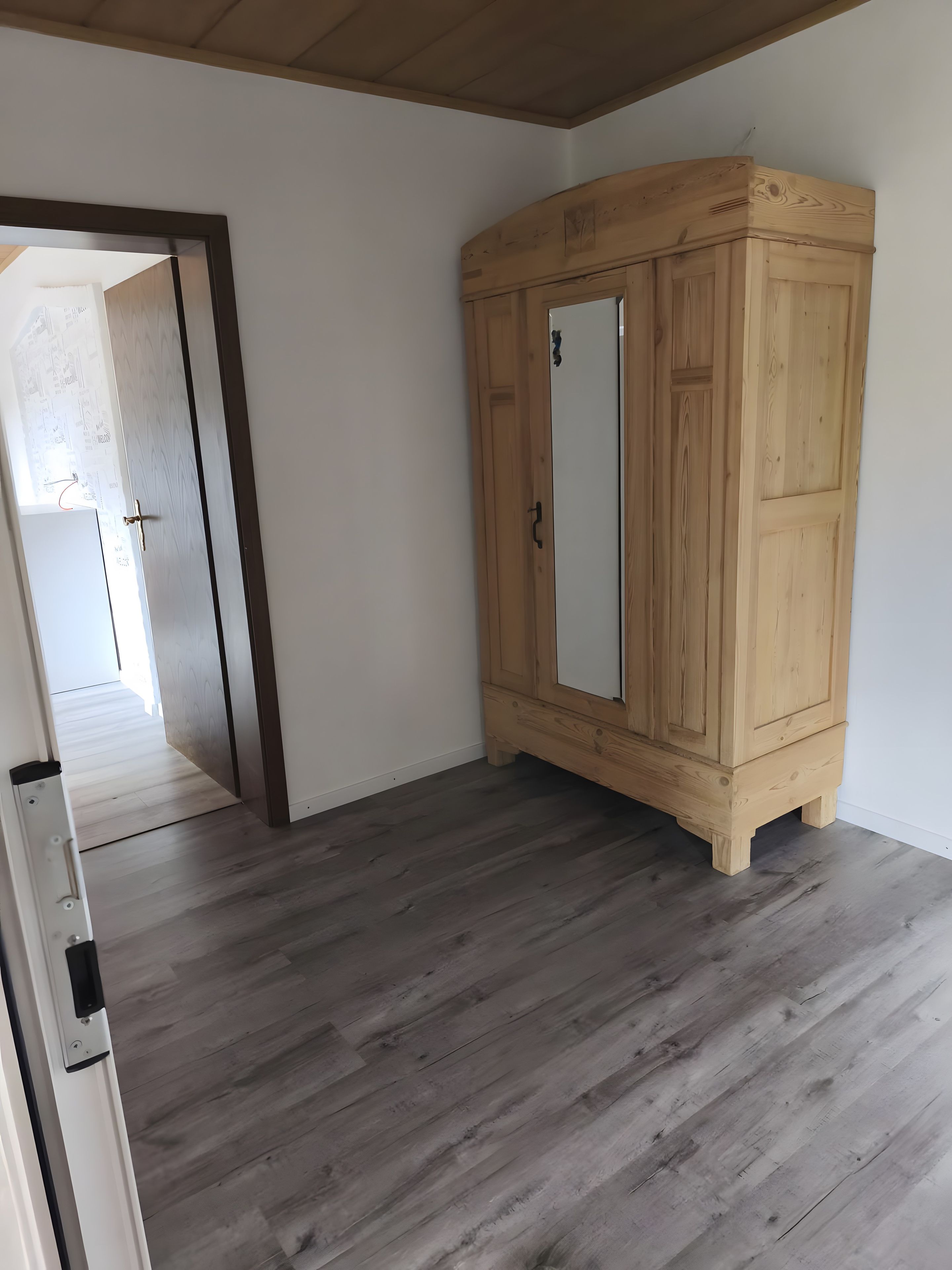 Ein Zimmer mit einem Holzschrank, einer weißen Tür und Holzboden.