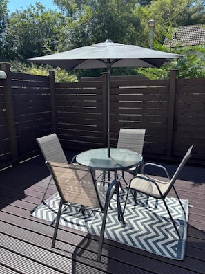 A patio with a round table and chairs, an umbrella, and a chevron-patterned rug. - House Sleeps 4 With Enclosed Garden (Oban)
