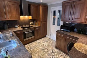 A kitchen with wooden cabinets, a stainless steel sink, a microwave, and a patterned floor. - House Sleeps 4 With Enclosed Garden (Oban)