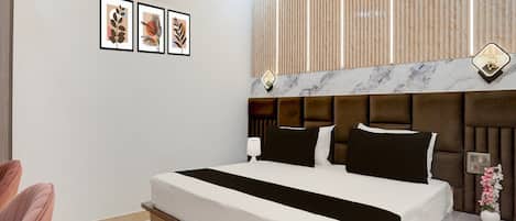 A modern hotel room with a large bed, a bedside table with a lamp, and a wall-mounted air conditioner.
