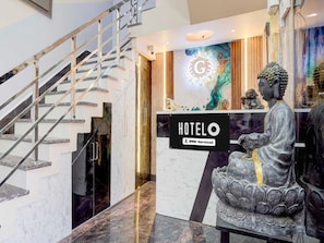 A hotel reception area with a marble staircase, a Buddha statue, and a sign indicating OYO-Serviced. - Classic G Grand Hotel (Sonepat)