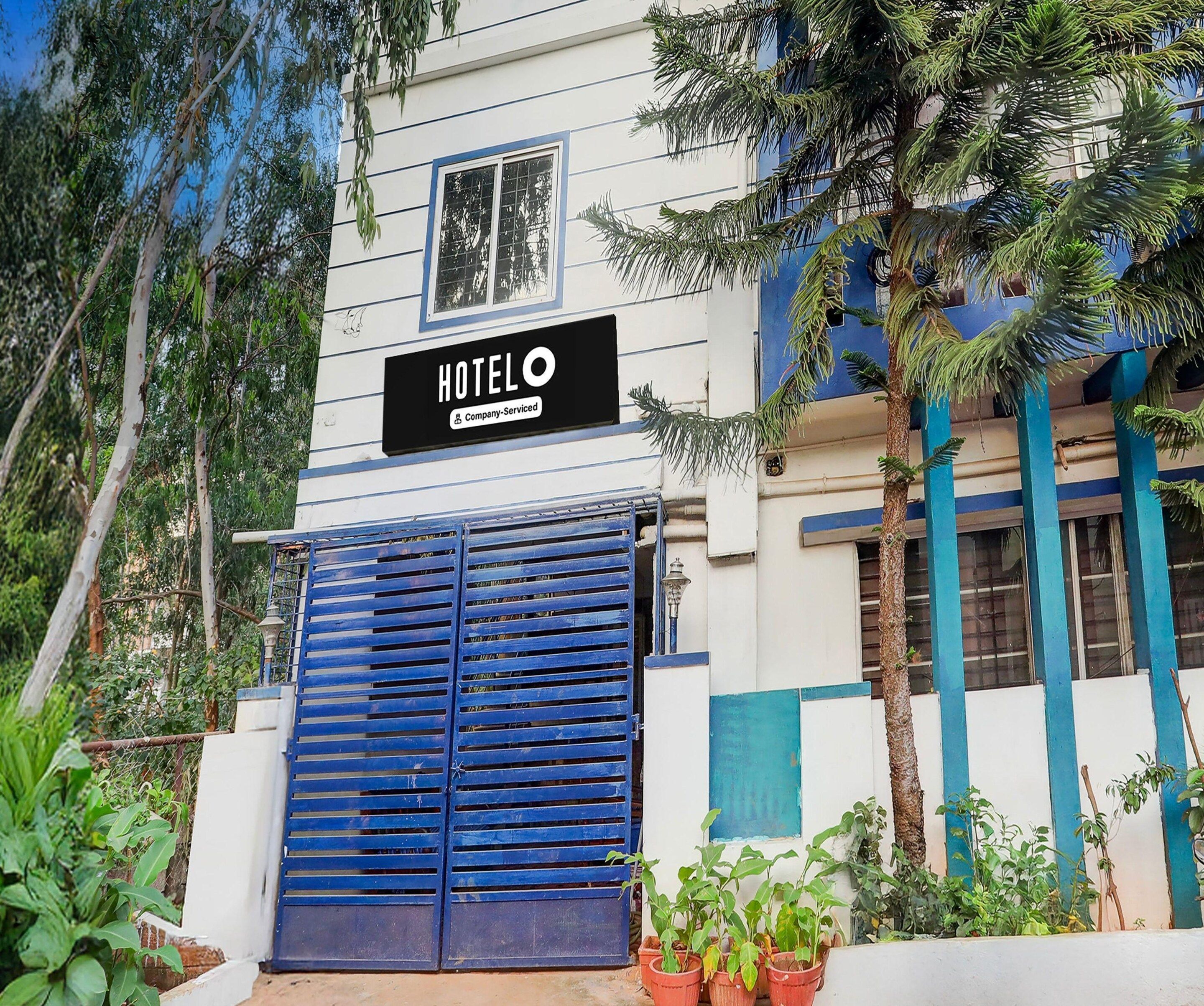 A hotel with a signboard, a blue gate, and potted plants.