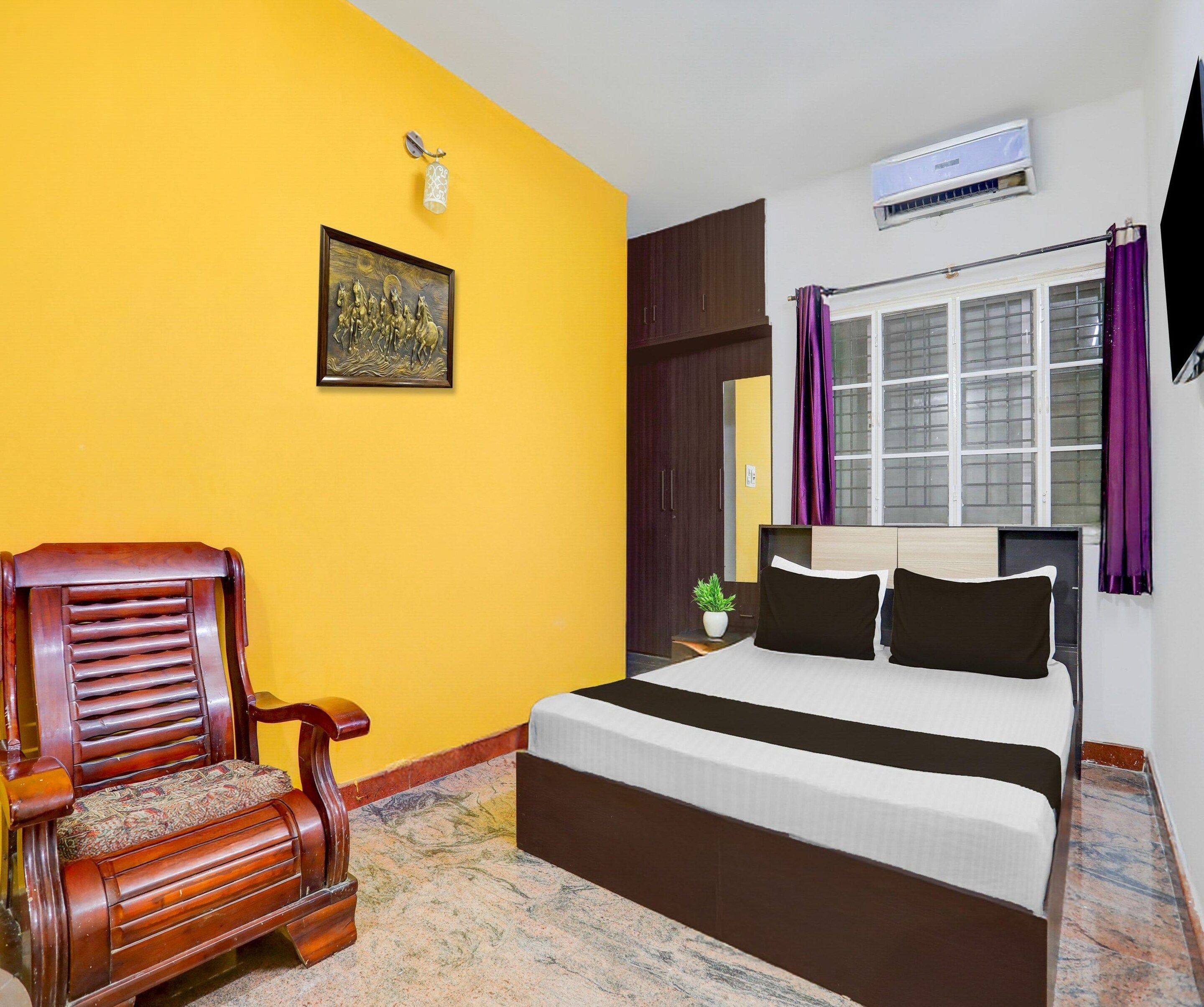 A bedroom with a bed, a chair, a picture on the wall, and an air conditioning unit.