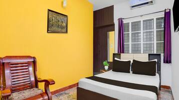 A bedroom with a bed, a chair, a picture on the wall, and an air conditioning unit.