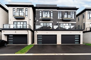 Un immeuble résidentiel moderne à plusieurs étages, doté de deux portes de garage, de grandes fenêtres et de balcons.