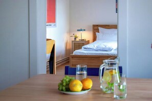 A hotel room with a wooden bed, a bedside table with a lamp, a small table with fruits and a pitcher, and a chair. - Thatched flat near Baltic Sea & golf course (Schashagen-Beusloe)