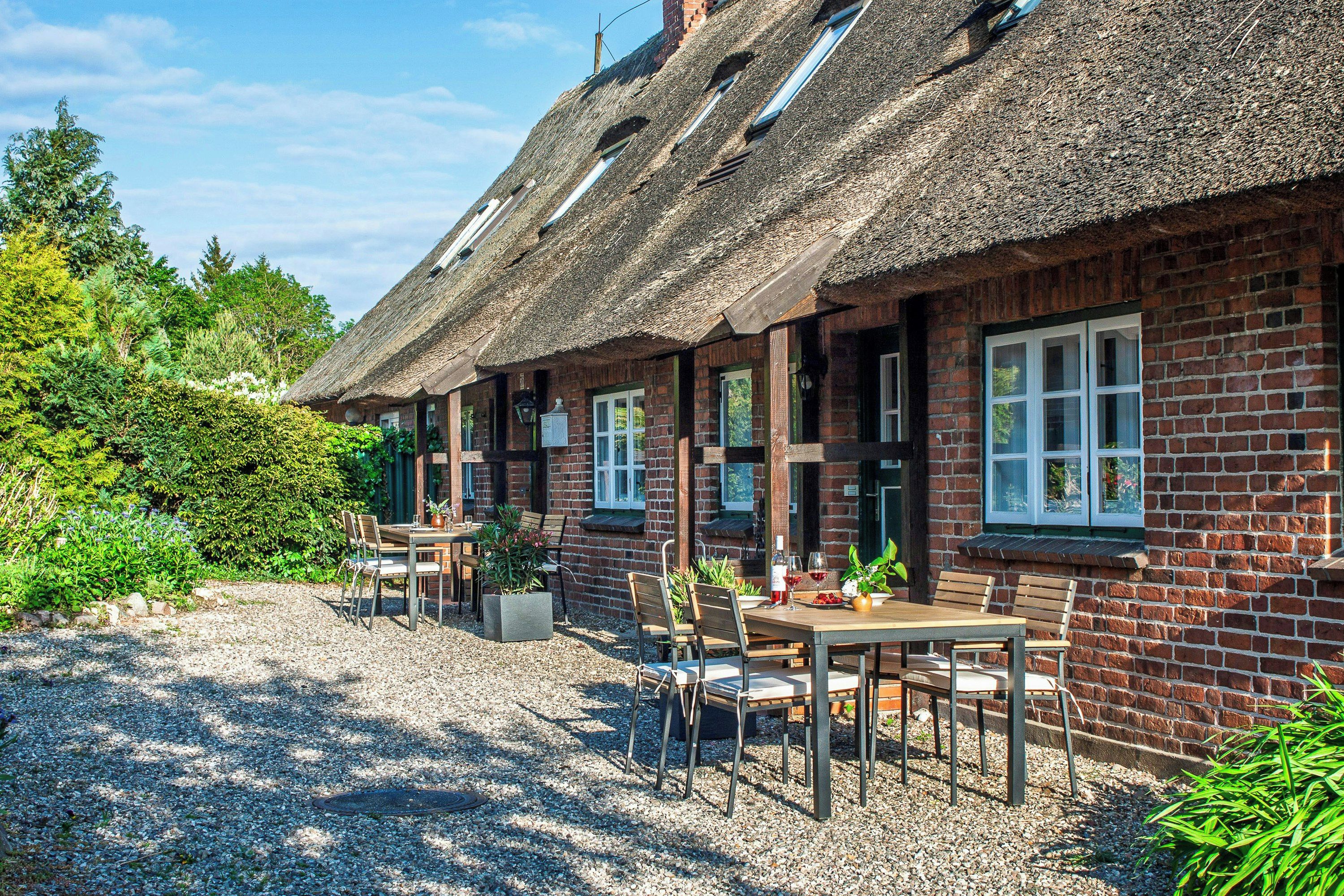 Ein traditionelles Reetdachhaus mit Kiespflaster-Terrasse und Sitzgelegenheit im Freien.