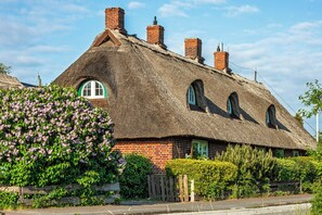 A traditional thatched-roof house with brick walls, multiple chimneys, and arched windows. - Thatched flat near Baltic Sea & golf course (Schashagen-Beusloe)