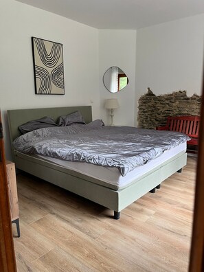A bedroom with a bed, a wall-mounted mirror, and a stone wall. - Cozy vacation home with private woods, surrounded by nature, near Houffalize (Houffalize)