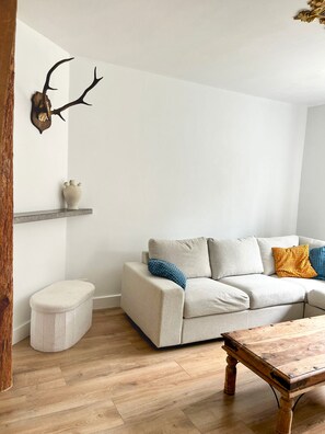 Een woonkamer met een bank, een bijzettafeltje, een houten vloer, een aan de muur bevestigd hertenhoofd en een plank met een vaas.