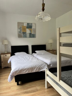 Een slaapkamer met een stapelbed, twee nachtkastjes met lampen, een kunstwerk aan de muur en een hanglamp.