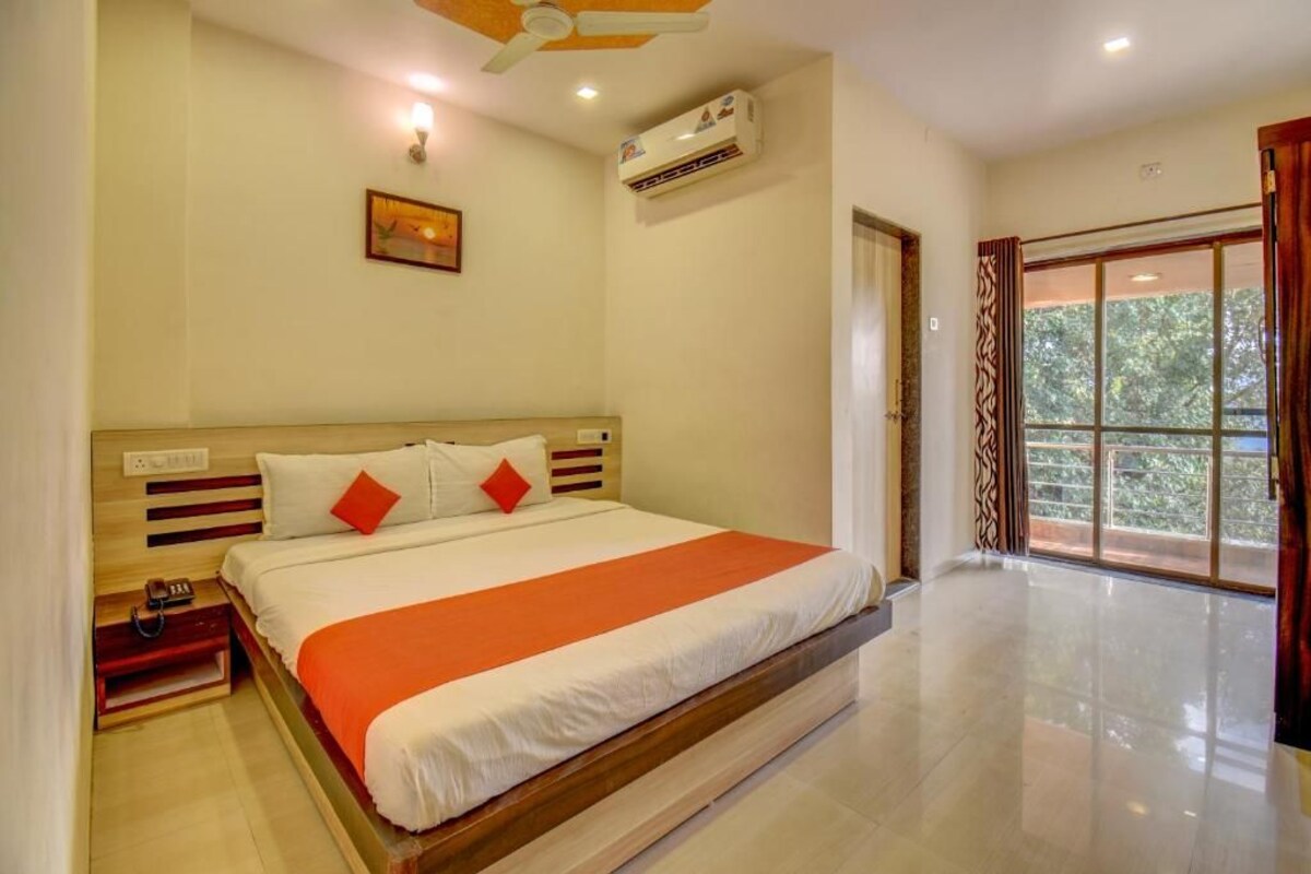 A bedroom with a large bed, a bedside table, an air conditioning unit, and a window with curtains.