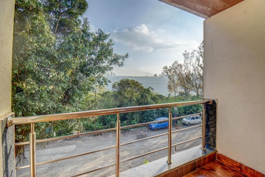 A balcony with a metal railing overlooking a road with parked cars and lush greenery.
