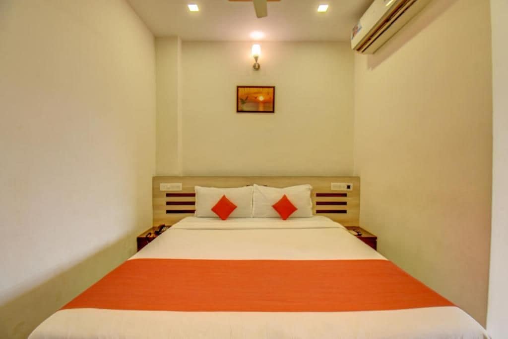 A hotel room with a bed, nightstands, a wall-mounted lamp, and an air conditioning unit.