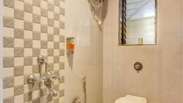 Un baño con pared de baldosas de cuadros, inodoro, ducha y espejo.