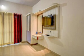 A hotel room with a wooden floor, a white sink with a mirror, a television mounted on the wall, and a red curtain. - JK Hotels & Spa, Mahabaleshwar  (Metgutad)