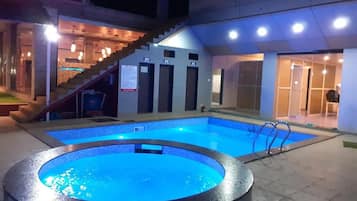 A swimming pool with a tiled edge, a staircase leading to an upper level, and a door with an emergency exit sign.