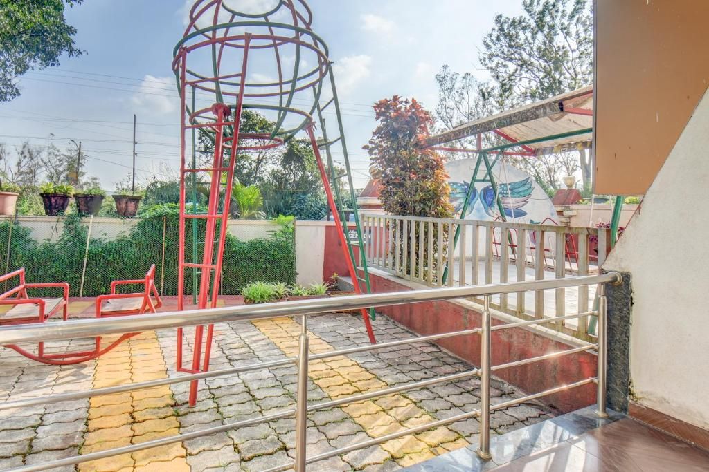Une aire de jeux avec une structure d’escalade rouge, une balançoire et un petit pont.