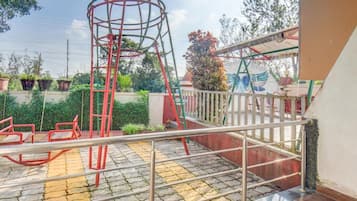 Une aire de jeux avec une structure d’escalade rouge, une balançoire et un petit pont.