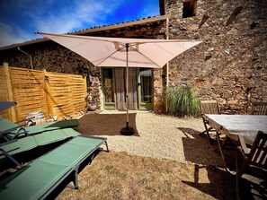 Un patio con mesa y sillas, una zona de estar cubierta y un muro de piedra.