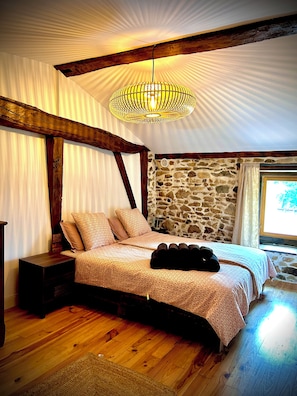 Un dormitorio con pared de piedra, vigas de madera, una cama con ropa de cama estampada y una lámpara colgante.