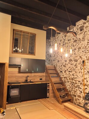 A kitchen with a wooden countertop, black cabinets, a built-in oven, and a stone wall.