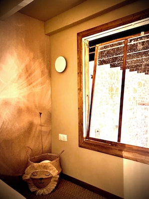 Una habitación con ventana, una lámpara de pared y una cesta decorativa.