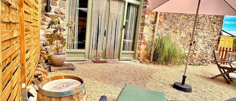 Un espacio al aire libre rústico con sillones de descanso, un barril de madera y una pared de piedra.