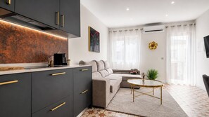 A modern kitchen with dark cabinets and a countertop, a beige sofa, a round coffee table, and a large window with sheer curtains. - Stay at Ruby's Boutique townhouse for 6– 3 terraces, 4 min walk to the beach (Fuseta)