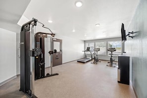 Une salle de sport équipée de matériel d’exercice, d’un tapis de course et d’un téléviseur fixé au mur.