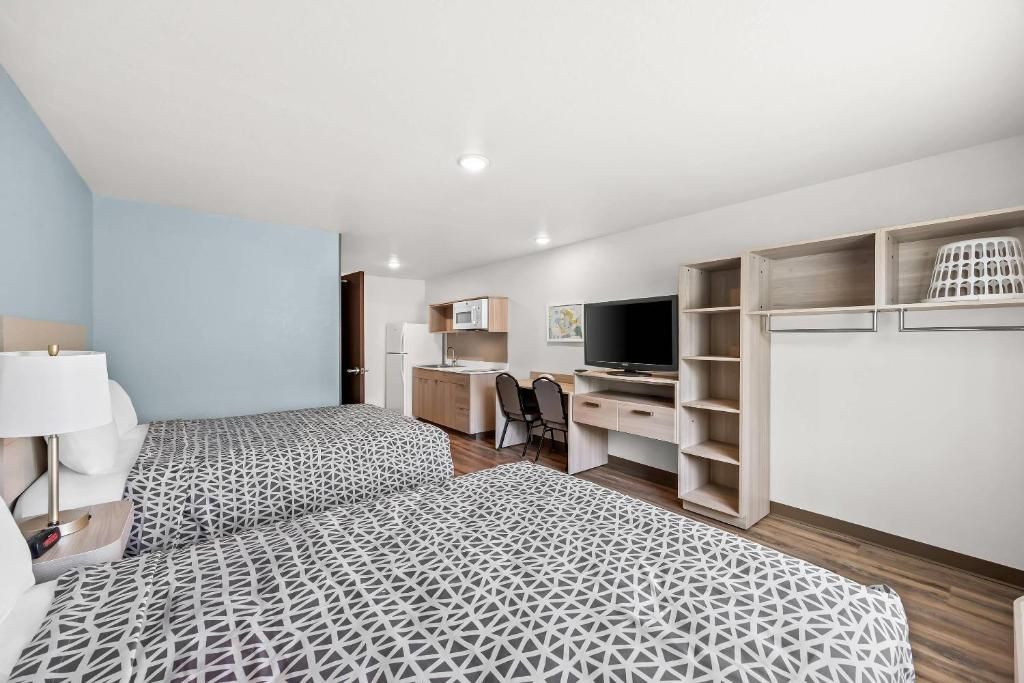 A hotel room with two beds, a desk, a television, and built-in shelving.