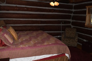 Ein Blockhaus-Interieur mit einem Bett, einem Sessel und einem Fenster.