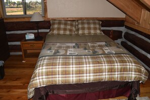 Ein Schlafzimmer in einer Blockhütte mit einem Bett, einem Nachttisch und einem Fenster.