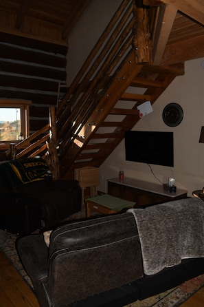 Ein gemütlicher Wohnbereich mit einer Holztreppe, einem Flachbildfernseher und einem Ledersofa.