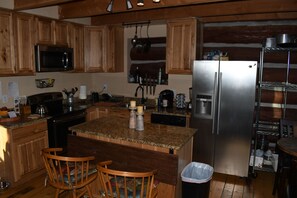 Una cocina con armarios de madera, refrigerador de acero inoxidable, encimeras de granito y una isla central con sillas.