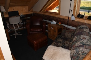 Ein gemütliches Zimmer mit braunem Ledersessel, einem Holzschrank, einer gemusterten Couch und einem Schreibtisch mit Stuhl.