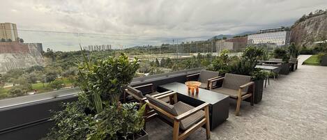 A rooftop terrace with outdoor seating, potted plants, and a view of the cityscape.