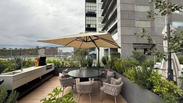 Une terrasse extérieure avec une table ronde et des chaises, un barbecue et une vue sur le paysage urbain.
