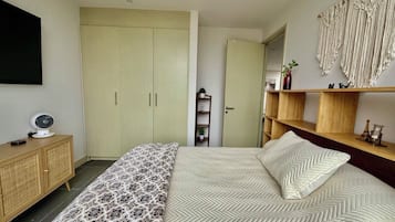 Een slaapkamer met een bed, kast, nachtkastje en een wandplank.