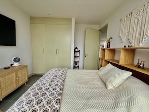 Et soveværelse med seng, garderobe, natbord og vægmonteret hylde.